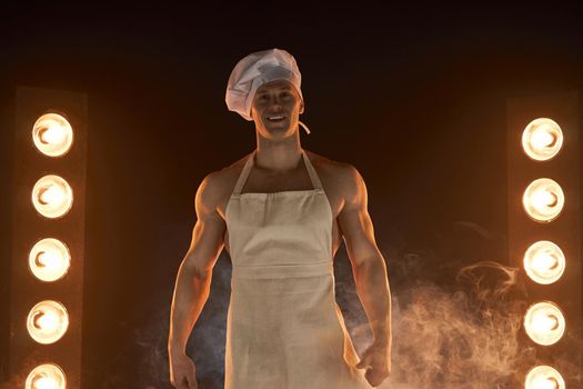 Portrait of muscular chef wearing white apron and cheef hat, posing on smoky background male housewife. husband in kitchen. brutal butcher.