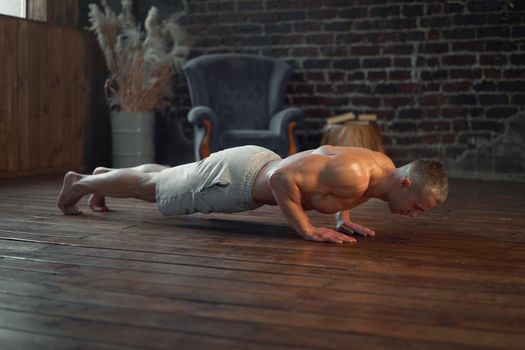 Endurance workout. Strong muscular man practicing push ups exercise at home interior Caucasian athlete do plank training indoors