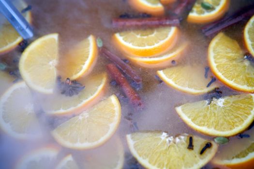 closeup of mulled wine citrus fruit, preparing in big old metal kettle on fire, above view, Traditional Christmas fair market beverage