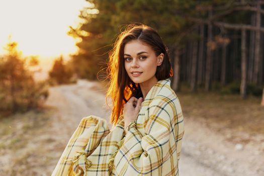 Pretty woman in the woods on the road with a blanket on her shoulders at sunset. High quality photo