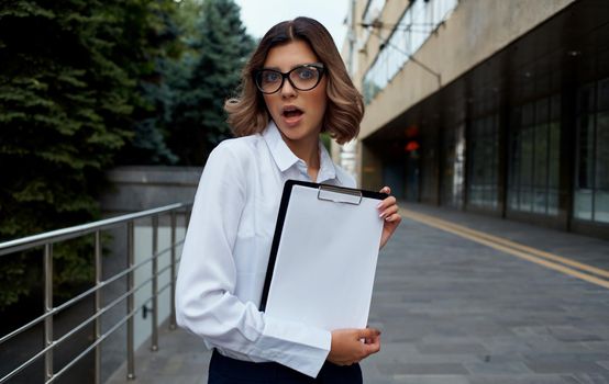 Happy business woman with documents near the building on the street in glasses and in a white shirt. High quality photo