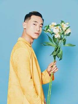 Side view of a guy with a bouquet of flowers in a yellow coat on a blue background. High quality photo