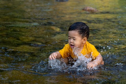 The boy was having fun playing in the water for the first time in the stream.
