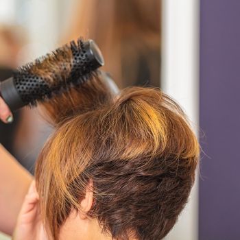 Woman makes hair by comb in beauty salon. Short haircut