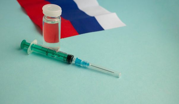 The vaccine and the injection syringe are on the small flag of Russia. For the prevention, immunization and treatment of coronavirus infection. The concept of medicine and healthcare.