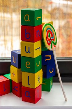 Tower of toy blocks with letters and numbers forming the word "abuela" (grandma in Spanish) and a colourful lollipop byf a window