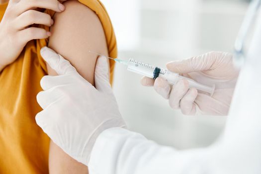 doctor in a medical gown giving a shot to the shoulder of a woman in a yellow t-shirt in a hospital close-up. High quality photo