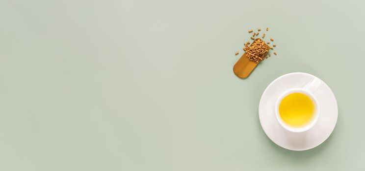 cup of buckwheat tea or kuqiaocha on light green background. Top view of healthy soba tea and groats in spoon on green paper background. Flat lay. Copy space. Long horizontal banner