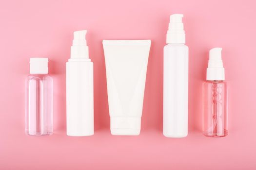 Set of cosmetic bottles for face cleansing, exfoliating, hydrating and anti aging treatment against pink background. Flat lay with a set of beauty products for daily use