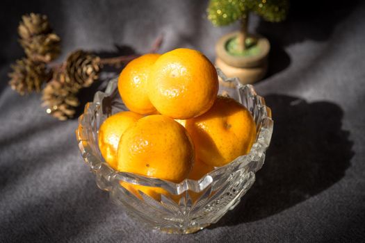 Crystal vase with a tangerine on grey background. Christmas accessories and elements.