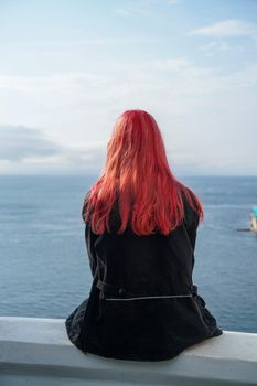 A girl with pink hair sits with her back against the sea. Vladivostok, Russia