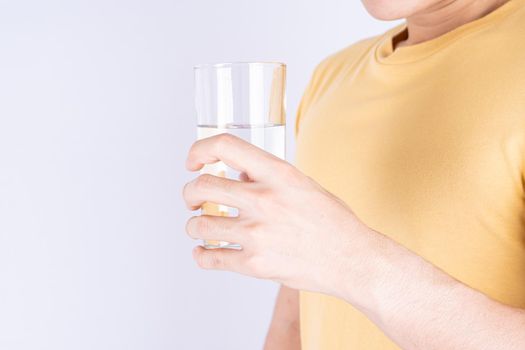 Man holding glass of water isolated grey background. Clean drinking water in clear glass.