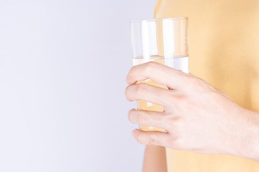 Man holding glass of water isolated grey background. Clean drinking water in clear glass.