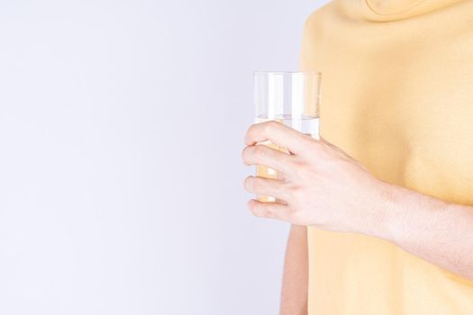 Man holding glass of water isolated grey background. Clean drinking water in clear glass.