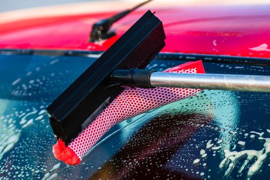 Washing and cleaning the front window of a car with mop in self service car wash station, close up isolated.