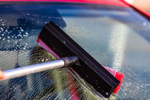 Washing and cleaning the front window of a car with mop in self service car wash station, close up isolated.