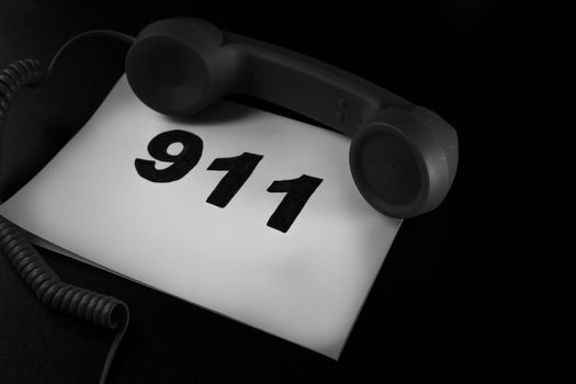 Call 911 and emergency call concept, text 911 on paper and phone isolated on black.