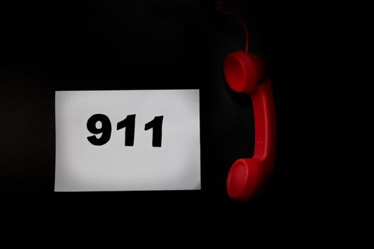 Call 911 and emergency call concept, text 911 on paper and phone isolated on black.