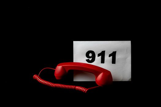 Call 911 and emergency call concept, text 911 on paper and phone isolated on black.