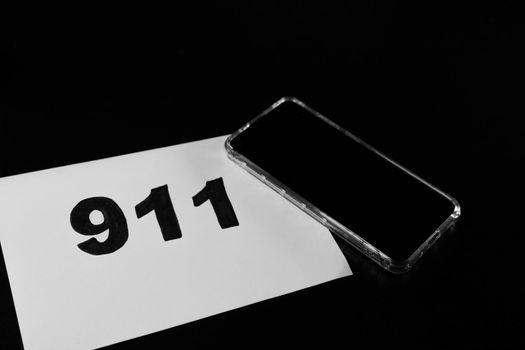 Call 911 and emergency call concept, text 911 on paper and phone isolated on black.