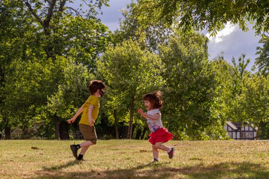 boy and a girl running in a park on a sunny summer day wearing a face mask