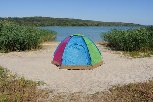 Nobody near camping tent located on sand bank river in local hike travel solitude nature. Colourful dome tent on lake shore or camping equipment travel. Tourist tent for trekking eco travel or fishing
