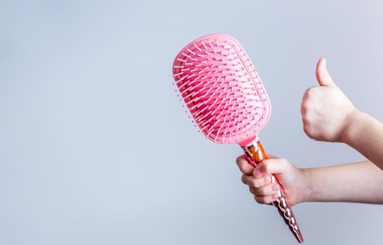 Beautiful pink comb brush in the hand of a girl with thumb up on white background. Women's Hair Care Accessories. Side view
