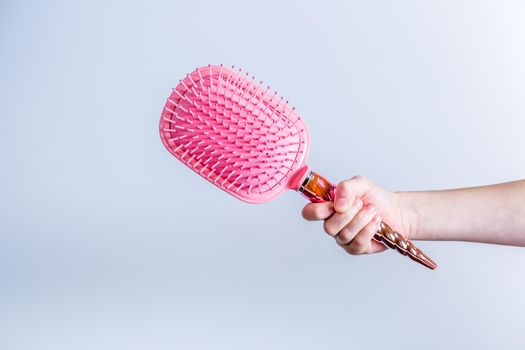 Beautiful pink comb brush in the hand of a girl on a white background with copy space