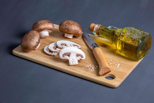 Still life of mushrooms on a cutting board knife and a bottle with olive oil, side view