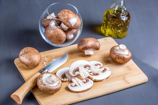 Royal champignons, Parisian champignons, chopped mushrooms on bamboo wooden chopping board, close-up. Dark wooden background. Side view.