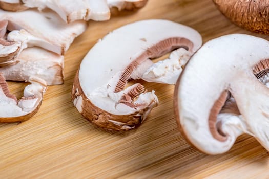 Royal champignons, Parisian champignons, chopped mushrooms on bamboo wooden chopping board, close-up. Dark wooden background. Side view.