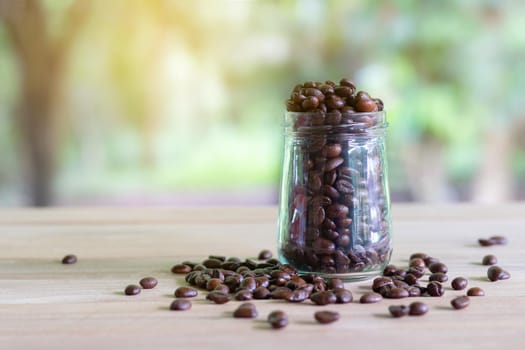 Roasted coffee beans in glass bottles placed on the table with nature background.