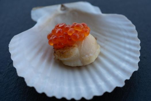 Scallop on a shell with a cap of red caviar. Seafood delicacy.