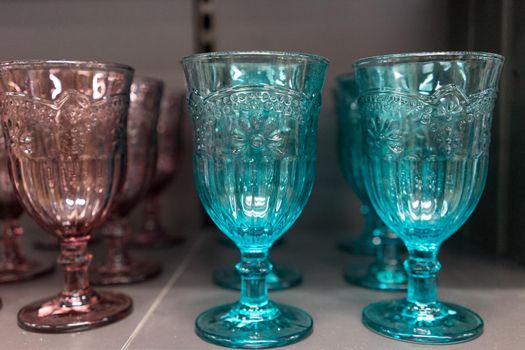 High notched wine glasses colored glass, standing on a shelf.