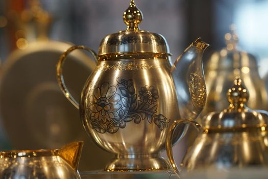 Silver teapot with blackened floral patterns on blurred background.