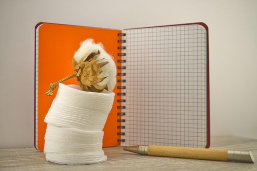 Raw cotton boll and stack of makeup remover pads placed in front of of wire bound notepad. Concept of natural cotton products