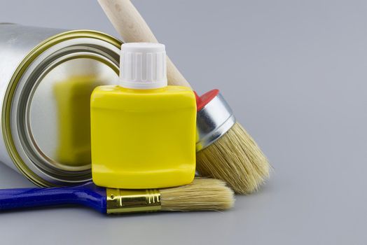 DIY, decorating or renovations concept with a still life with assorted clean paint brushes and unlabeled tin of paint over a grey background