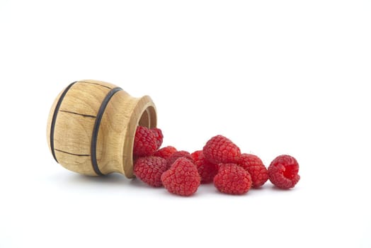 Heap of red ripe raspberry berries fall out of a wooden container isolated on white background