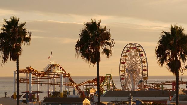 Classic ferris wheel, amusement park on pier in Santa Monica pacific ocean beach resort. Summertime California aesthetic, iconic view, symbol of Los Angeles, CA USA. Sunset golden sky and attractions.