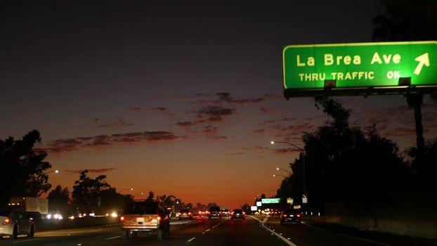 View from the car. Los Angeles busy freeway at night time. Massive Interstate Highway Road in California, USA. Auto driving fast on Expressway lanes. Traffic jam and urban transportation concept