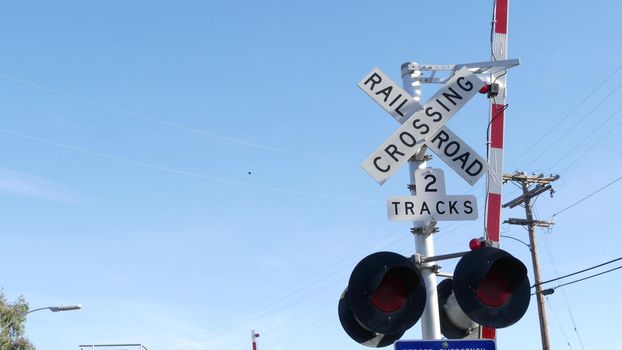 Level crossing warning signal in USA. Crossbuck notice and red traffic light on rail road intersection in California. Railway transportation safety symbol. Caution sign about hazard and train track.