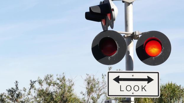 Level crossing warning signal in USA. Crossbuck notice and red traffic light on rail road intersection in California. Railway transportation safety symbol. Caution sign about hazard and train track.