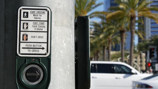 Traffic light button on pedestrian crosswalk, people have to push and wait. Traffic rules and regulations for public safety in USA. Zebra street crossing on road intesection in San Diego, California.