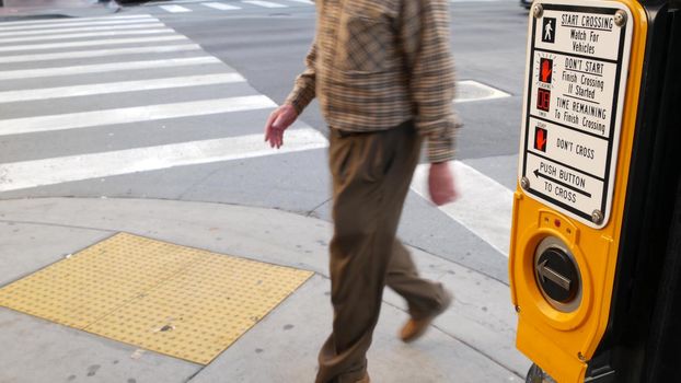 Traffic light button on pedestrian crosswalk, people have to push and wait. Traffic rules and regulations for public safety in USA. Zebra street crossing on road intesection in San Diego, California.