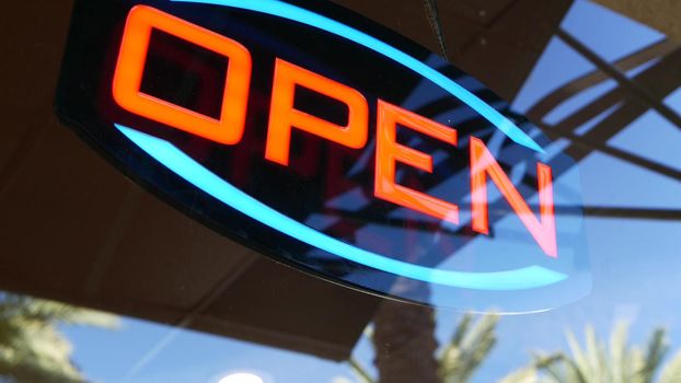 Open neon sign glowing in the dark. Vivid retro styled text at entrance on glass window. Colorful electric banner selective focus close up. Light bulbs radiance at night. Shiny illuminated lettering.