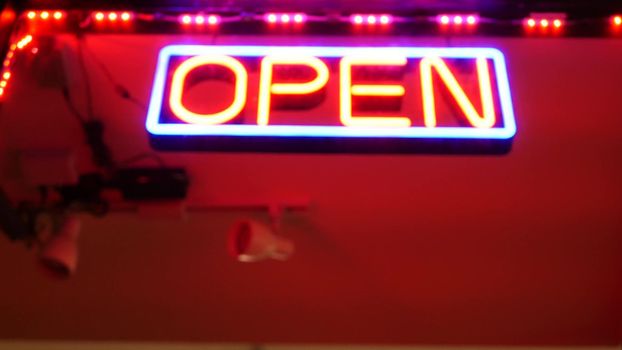 Open neon sign glowing in the dark. Vivid retro styled text at entrance on glass window. Colorful electric banner selective focus close up. Light bulbs radiance at night. Shiny illuminated lettering.