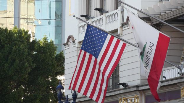 Flags of California and United States waving on flagpole in Gaslamp, center quarter of San Diego. Bear emblem of Republic and Star-Spangled Banner on flagstaff. Symbol of ptriotism and government.