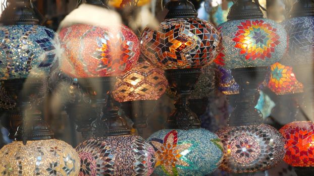 Colourful turkish lamps from glass mosaic glowing. Arabic multi colored authentic retro style lights. Many illuminated moroccan craft lanterns. Oriental islamic middle eastern decor. Shiny folk shop.