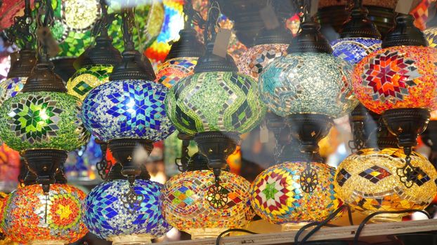 Colourful turkish lamps from glass mosaic glowing. Arabic multi colored authentic retro style lights. Many illuminated moroccan craft lanterns. Oriental islamic middle eastern decor. Shiny folk shop.