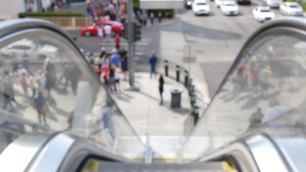 Perspective view thru escalator, defocused unrecognizable group of people on road intersection crosswalk on Strip of Las Vegas, USA. Anonymous blurred pedestrians on walkway in crowded urban downtown.
